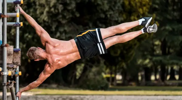 Mężczyzna wykonuje planche na drążku, demonstrując siłę i kontrolę. To dowód, że kalistenika czy siłownia – liczy się trening!